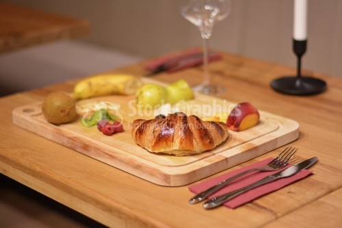 A croissant and fruit on a wooden platter.