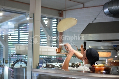 A pizza maker throws up a pizza dough. The guy is standing with his back, his face is not visible. The interior of the restaurant.