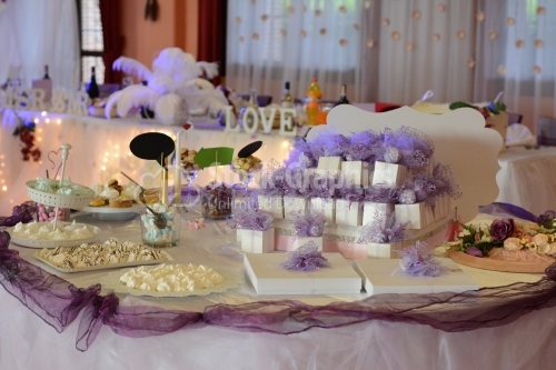 Candy bar on wedding party with a lot of different candies, cupcakes, souffle and cakes. Decorated in purple and white colors, indoor.