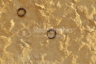 Cement wall with yellow plaster and two iron rings