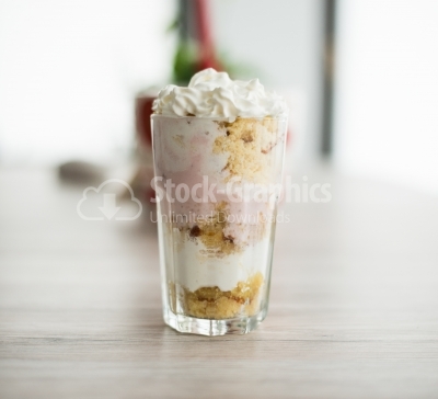 Dessert in glass with lots of whipped cream, on a wooden backgro