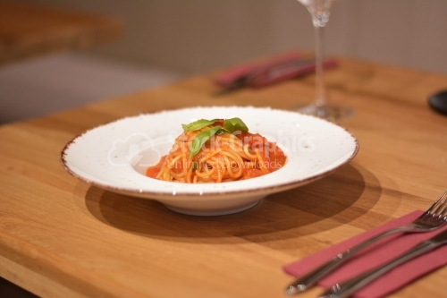 Detail of fresh pasta topped with tomato sauce and leaves of basil.
