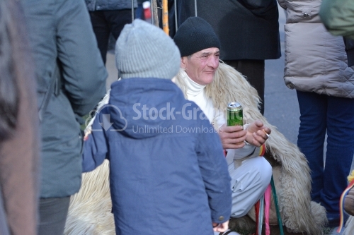 Old man dressed in a shepherd, drinking beer and smoking, at the winter festival. Authentic traditional from Romania