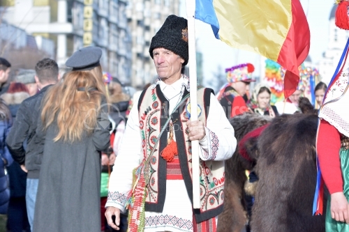 Old man dressed in Romanian national costume. He holds the flag of Romania in his hand.