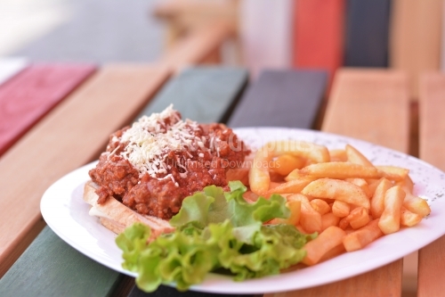 Plate with minced meat sauce on toast, french fries and salad.