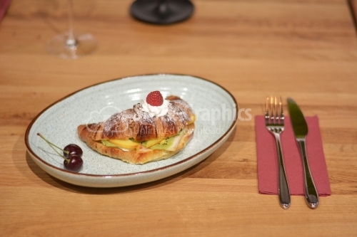 Plate with sweet croissant and fruit slices on table.