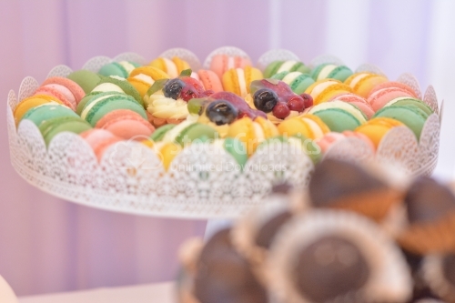 Platter with colorful macarons and mini tarts with fruit and vanilla cream in the middle