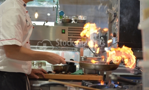 Seafood cooked with flame in a professional kitchen. The chef is photographed from one side.