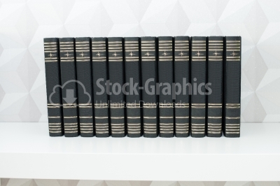Stack of books with hard covers on a white shelf front view.