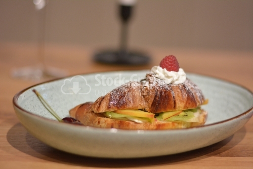 Sweet croissant and fruit slices on table, closeup.