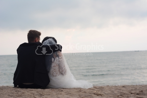 The bride and groom look back as they sit on the beach.