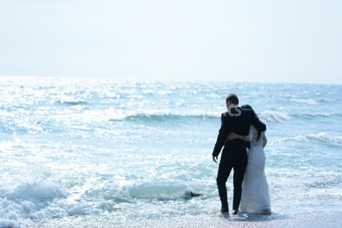 The embraced bride and groom enter the waves of the sea.