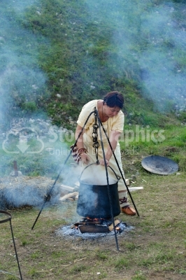 Woman cooking on campfire at festival, food prepared in cauldron